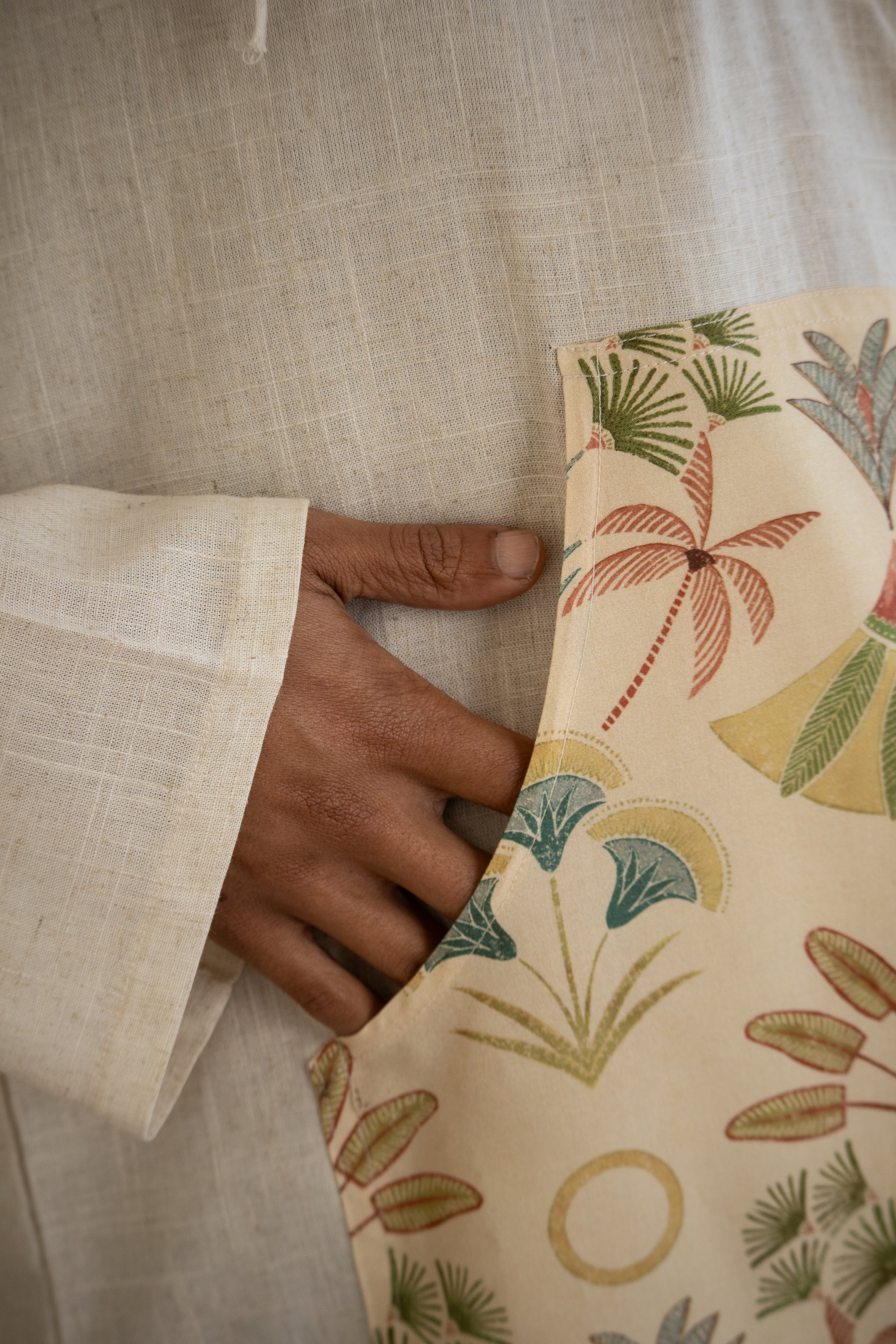 Hand holding a patterned pouch with palm tree design on a textured fabric background