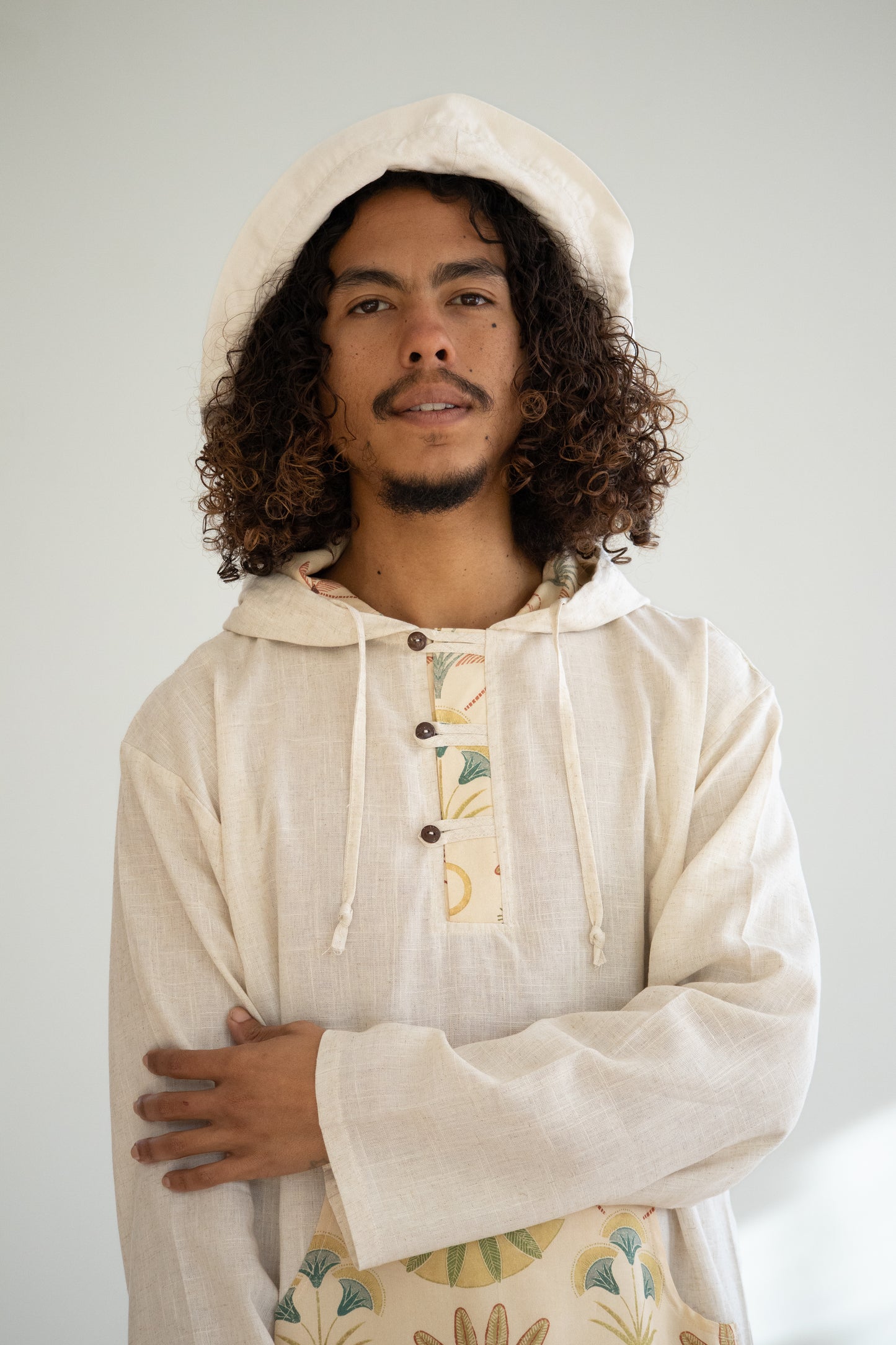 Man wearing a beige hoodie with floral patterns on a plain background